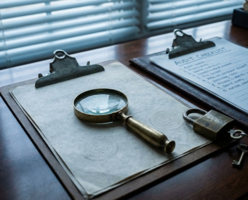 audit-checklist-beveiliging-documenten-bureaujpg - Hoek en Blok.IT - Hoek en Blok.IT Vergrootglas op officiële documenten met beveiligingszegels, koperen hangslot en sleutel op executive bureau in ochtendlicht