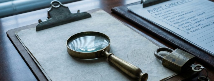 Vergrootglas op officiële documenten met beveiligingszegels, koperen hangslot en sleutel op executive bureau in ochtendlicht