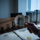 bedrijfsclassificatie-regelgeving-vergrootglas-kantoorjpg - Hoek en Blok.IT Vergrootglas boven miniatuurgebouwen op vergadertafel met officiële documenten, blauwe verlichting en professionele sfeer