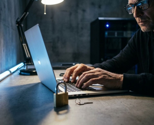 Hangslot en sleutel naast laptop terwijl cybersecurity-professional typt, blauw licht werpt schaduwen in moderne kantooromgeving