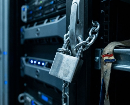 Metalen hangslot beveiligt ketting rond serverrack in datacenter met blauwe LED-lampjes en Nederlandse vlagpin