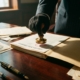Officiële hand drukt koperen inspectiestempel op compliance-documenten op mahonie bureau met dramatische belichting