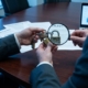 leveranciers-beveiliging-compliance-toezicht-auditjpg - Hoek en Blok.IT Beveiligingsprofessional onderzoekt keten van hangsloten met vergrootglas op vergadertafel, symboliseert toeleveringsketenrisico