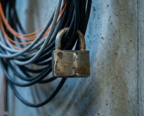 Stalen hangslot beveiligt bundel netwerkkabels en glasvezelkabels tegen betonnen muur in blauw industrieel licht