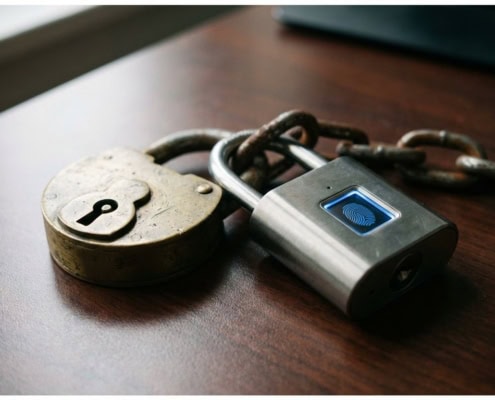 Verweerd koperen hangslot verbonden met modern titanium slot met vingerafdrukscanner door zware ketting op bureau
