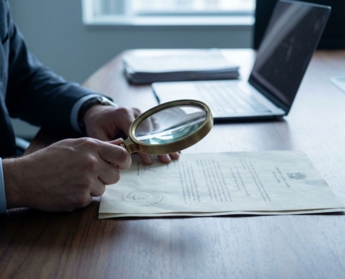 Zakelijke handen houden vergrootglas boven officieel document met zegel op donkere houten vergadertafel