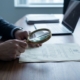 Zakelijke handen houden vergrootglas boven officieel document met zegel op donkere houten vergadertafel