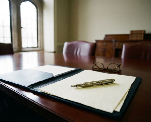 zakelijke-documenten-boardroom-pen-contractjpg - Hoek en Blok.IT - Hoek en Blok.IT Sierlijke vulpen op officiële documenten met zegel in elegante directiekamer, leesbril en zacht daglicht door hoge ramen.