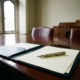 zakelijke-documenten-boardroom-pen-contractjpg - Hoek en Blok.IT Sierlijke vulpen op officiële documenten met zegel in elegante directiekamer, leesbril en zacht daglicht door hoge ramen.